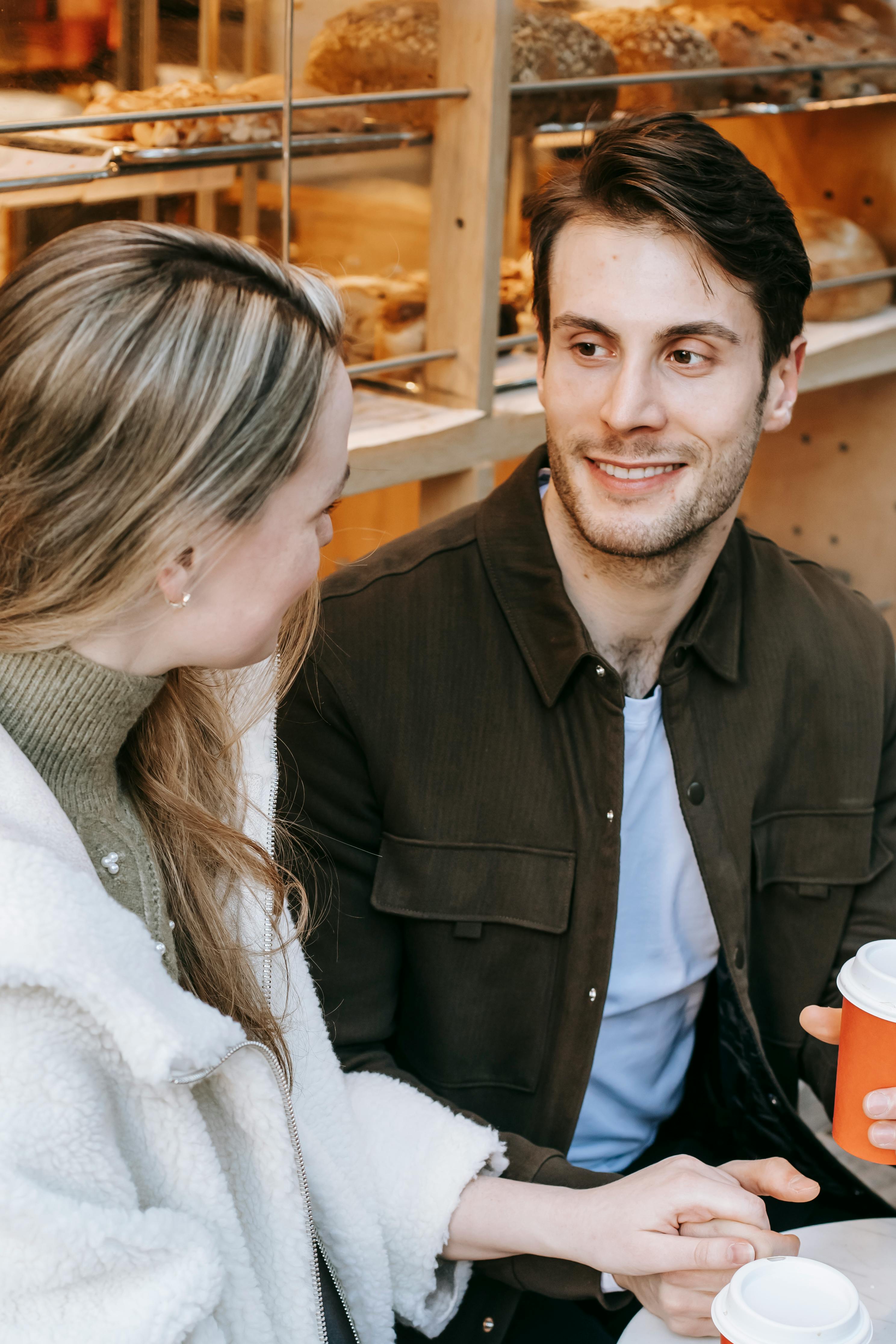 happy young couple chatting with takeaway coffee and holding hands