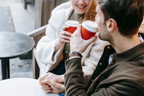 Crop lady and guy communicating while drinking takeaway beverages and holding hands