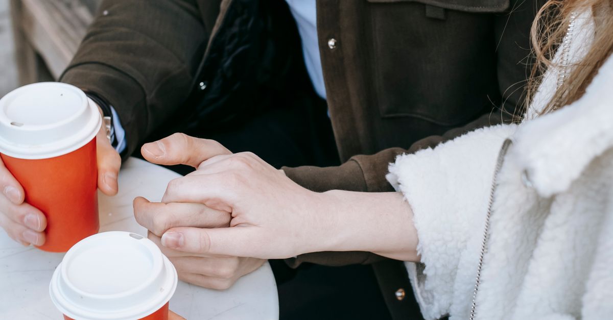 Rüyada Sevgiliyle Kahve İçmek: Anlamları ve İpuçları - Rüya Tabiri ve Anlamı - From above crop faceless man sitting at white table and holding hands with girlfriend while drinking coffee in red paper cups outdoors