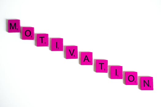 Pink Scrabble tiles spell out 'motivation' on a white background, creating a colorful inspirational image.