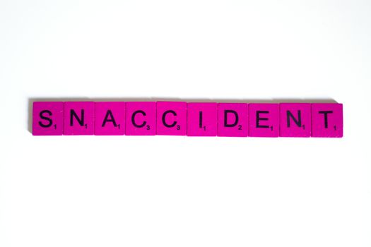 Pink letter tiles arranged on a white background spelling 'Snaccident' in a playful flat lay. — photo by Anna Tarazevich