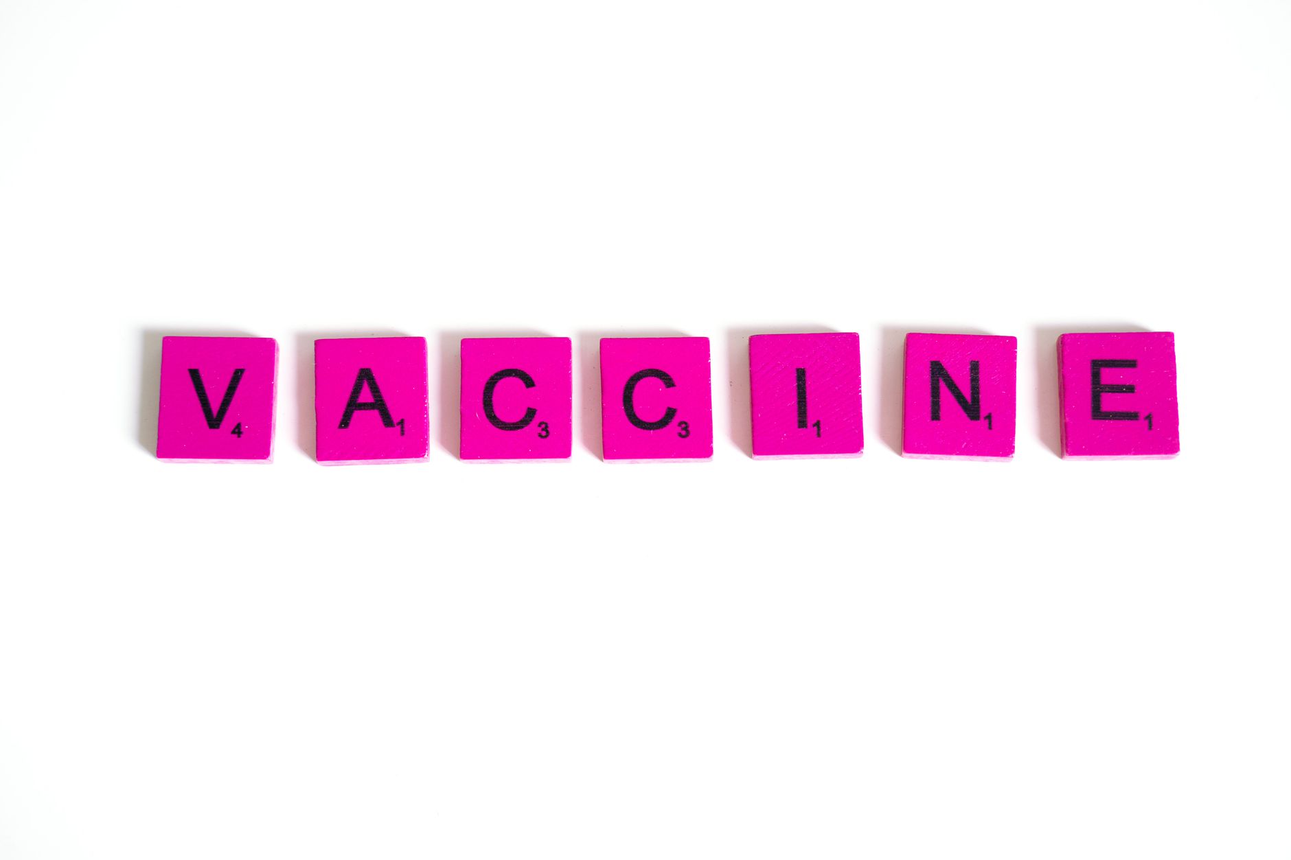 Pink scrabble tiles spelling 'VACCINE' on a white background, symbolizing immunization awareness.
