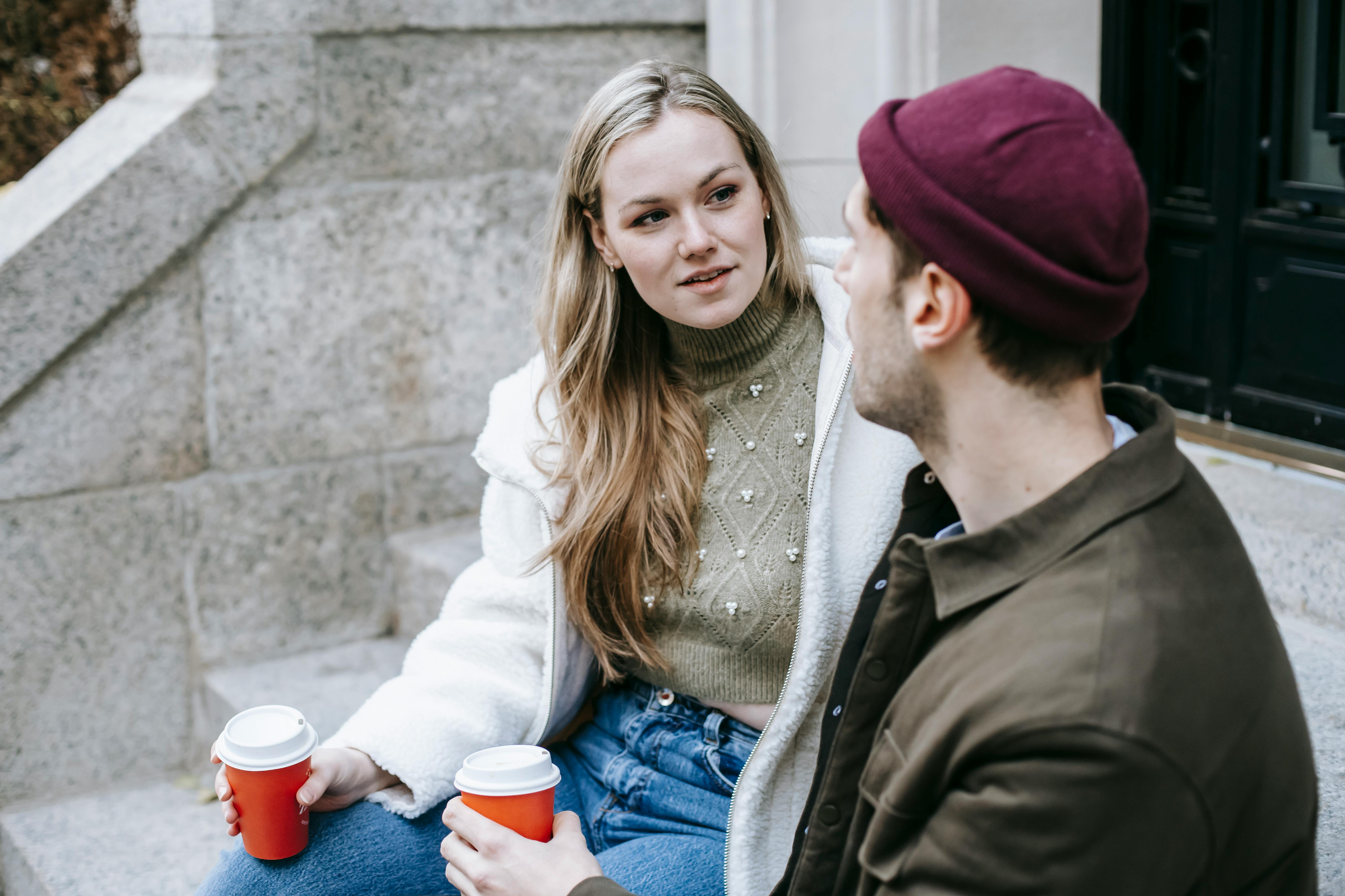 young couple talking and drinking beverages on stairs