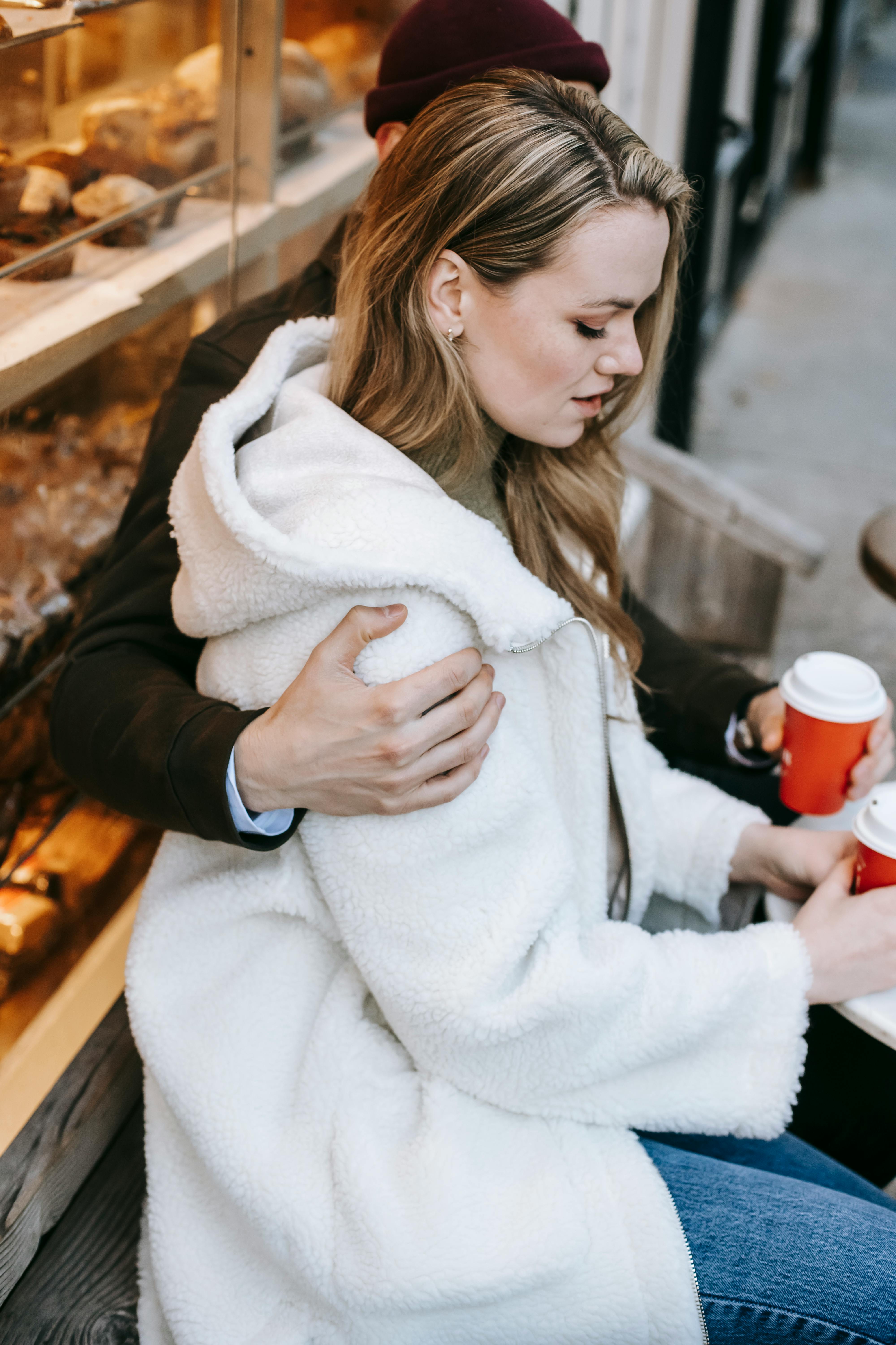 young couple cuddling and drinking hot beverage in coffee shop