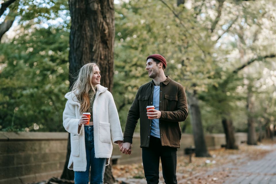 A young couple holding hands and drinking coffee while walking in an autumn park