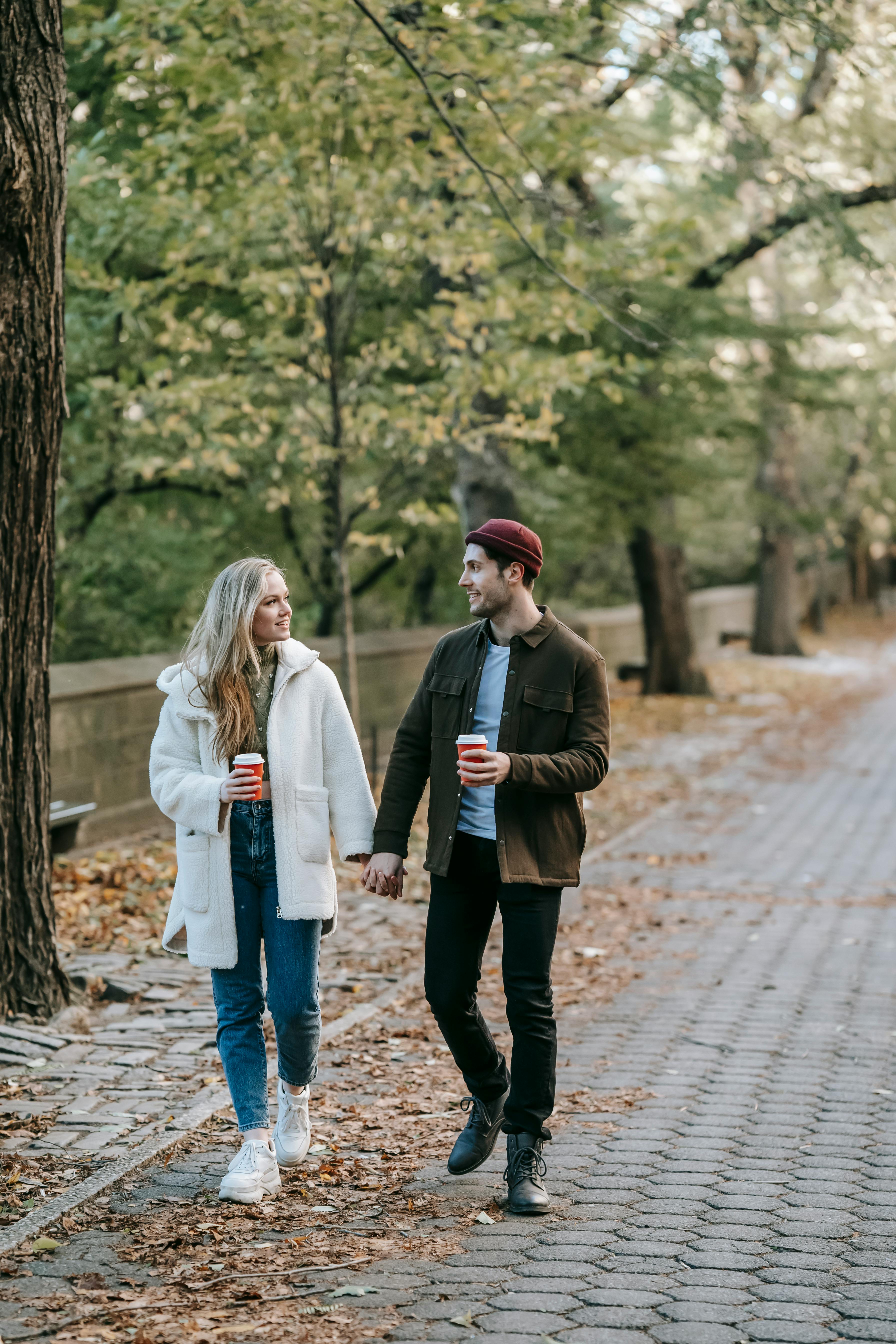 young couple strolling and chatting in park with coffee cups