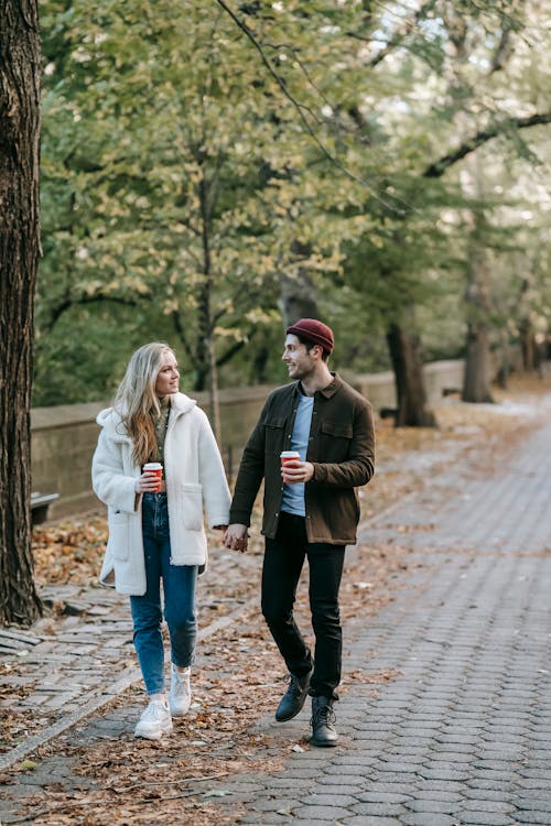 Free Young couple strolling and chatting in park with coffee cups Stock Photo