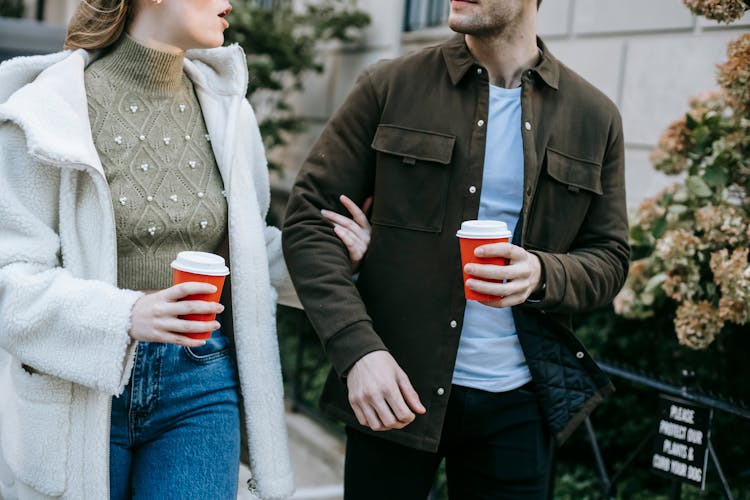 Crop Trendy Couple Chatting While Strolling On Street With Cups Of Takeaway Drink