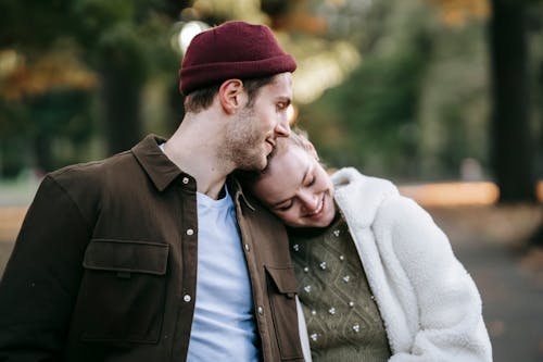 Free Romantic young couple in stylish warm clothes smiling and embracing during date on sunny autumn day Stock Photo