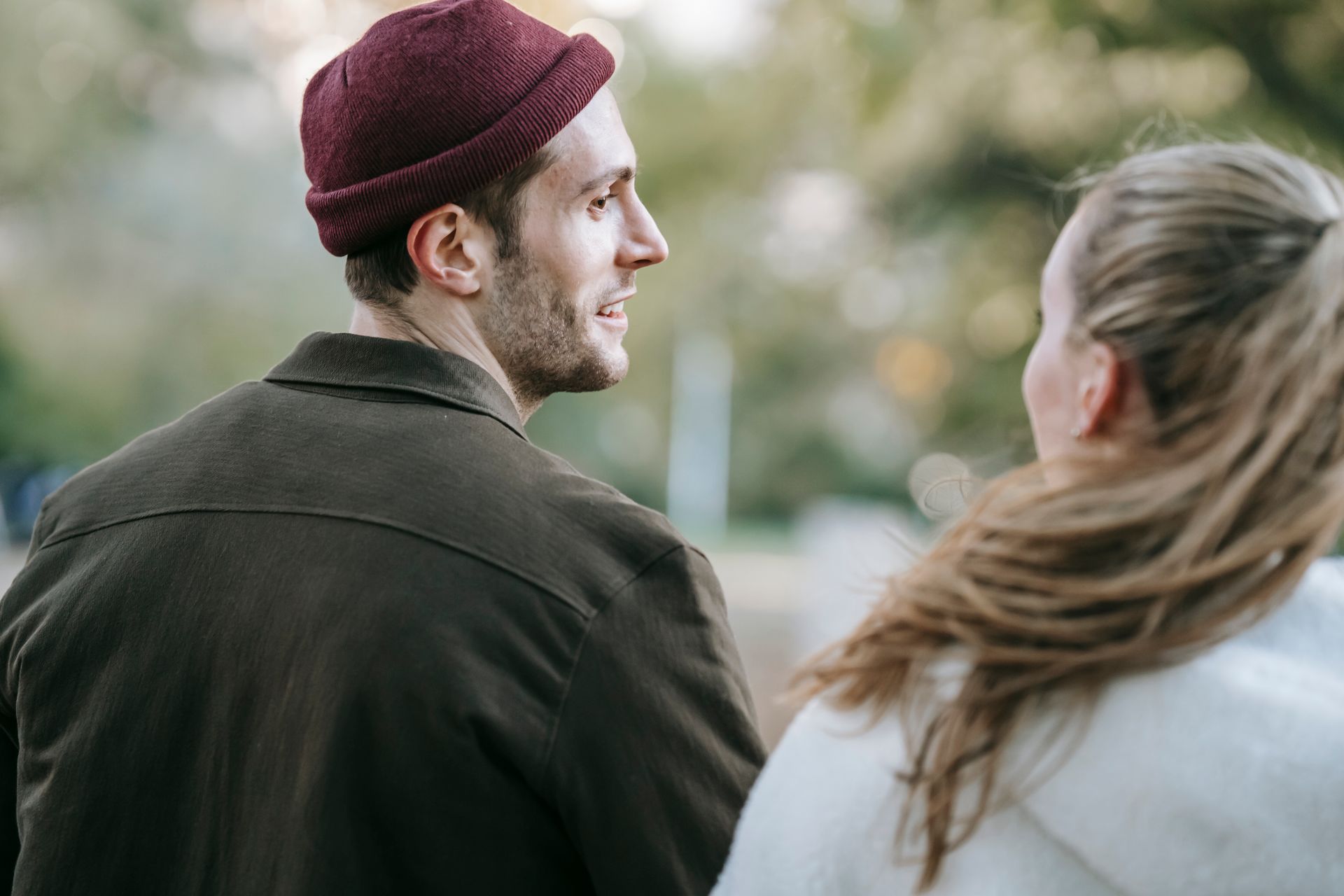 Back view of crop loving couple talking and smiling on blurred background of park