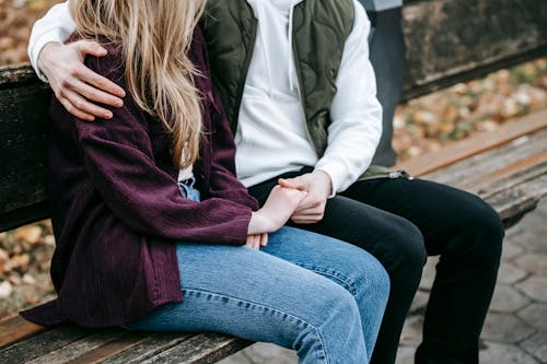 Free Crop anonymous tender young couple in casual stylish outfit cuddling and holding hands on wooden bench Stock Photo