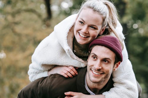 Cheerful smiling crop girlfriend embracing positive boyfriend on blurred background of green trees in park