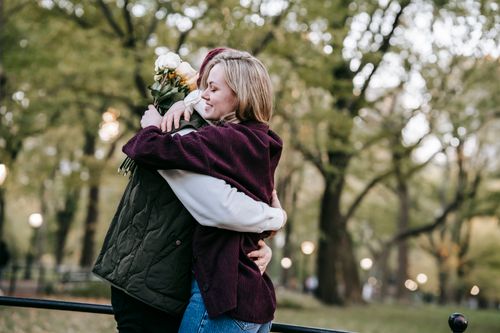 Free Side view of happy young couple in casual outfits with bouquet of flowers embracing in park Stock Photo