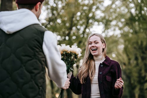 Loving boyfriend giving bouquet of flowers as present to happy girlfriend with long hair in park