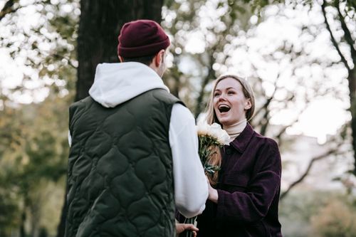 Free Loving boyfriend in hat giving bunch of roses as gift to happy girlfriend with long hair in casual warm clothes in park Stock Photo