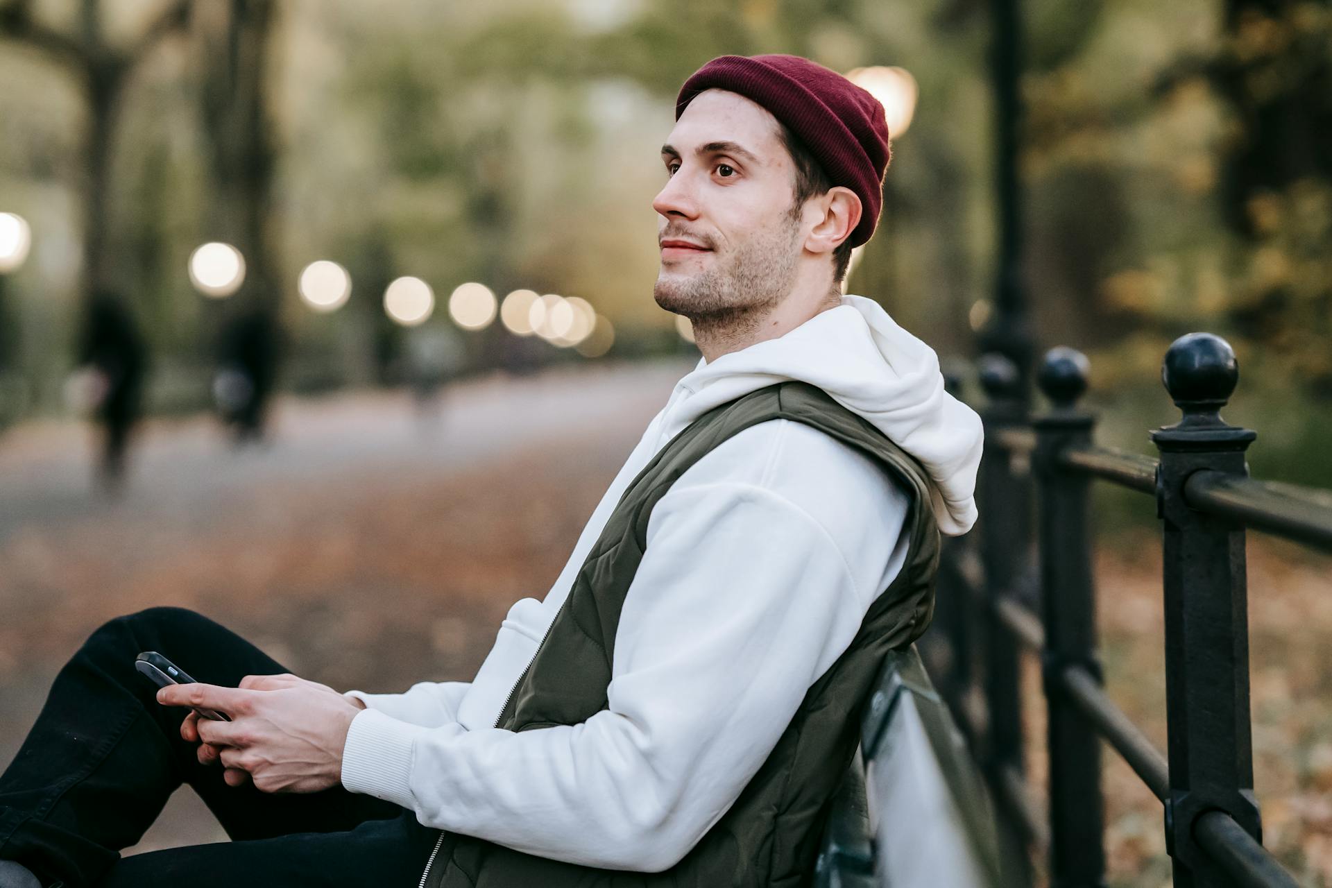 A young man enjoying a peaceful moment on a park bench during autumn, gazing away with a phone in hand.