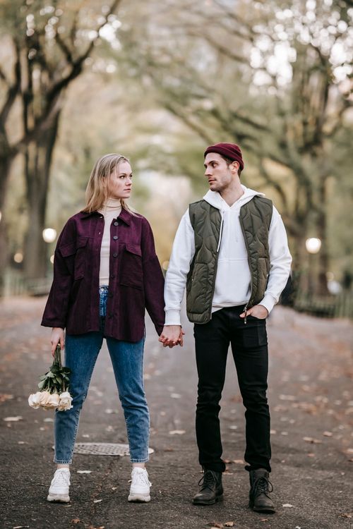 Free Full body of couple with fresh bouquet of white roses holding hands and looking at each other in park Stock Photo