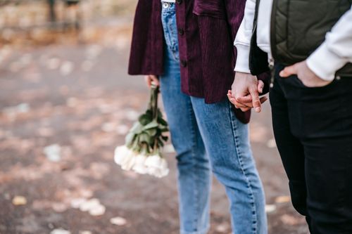 Free Crop anonymous couple with fresh white roses holding hands on blurred background of park Stock Photo