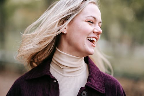 Cheerful female with flying hair and eyes closed laughing on blurred background of park