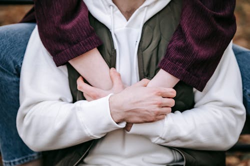 Crop anonymous woman embracing male beloved in casual apparel while holding hands in daytime