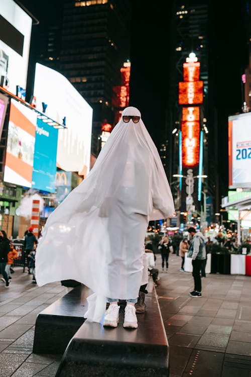 Unrecognizable person in ghost costume on illuminated street at night