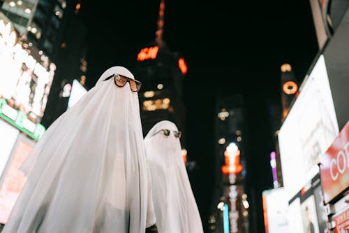 Unrecognizable couple in ghost costumes on illuminated street