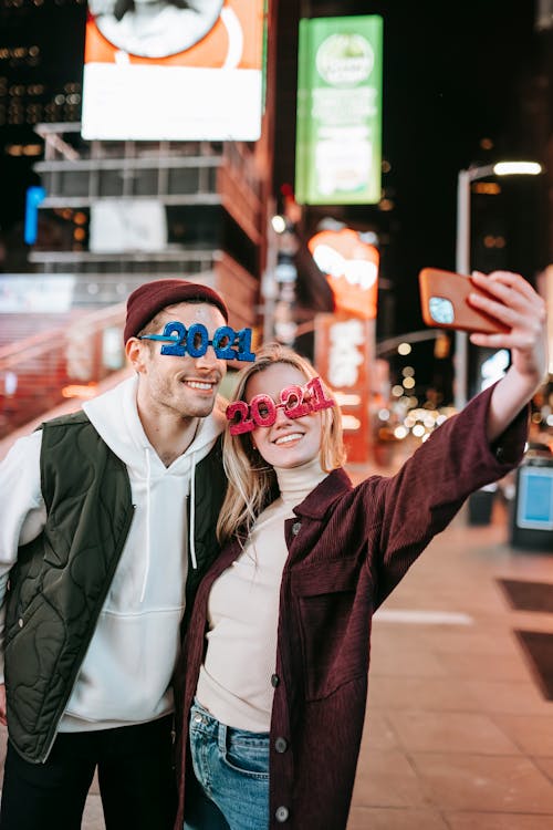 Cheerful couple in trendy glasses taking selfie on street