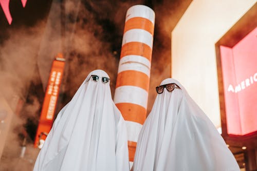 Unrecognizable couple in ghost costumes on night street with buildings