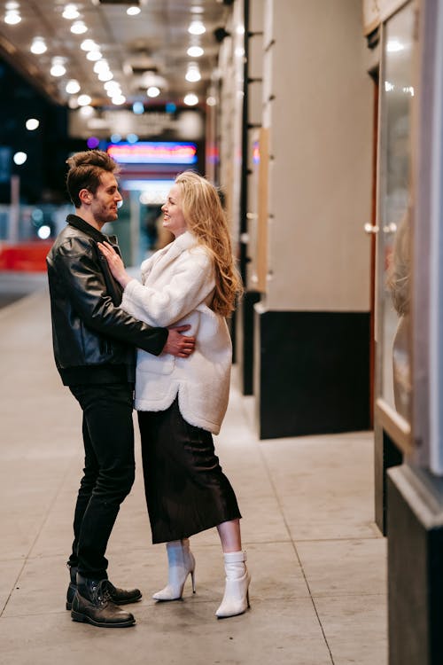 Side view full body of romantic couple looking at each other and embracing while standing in subway hall during date on evening time