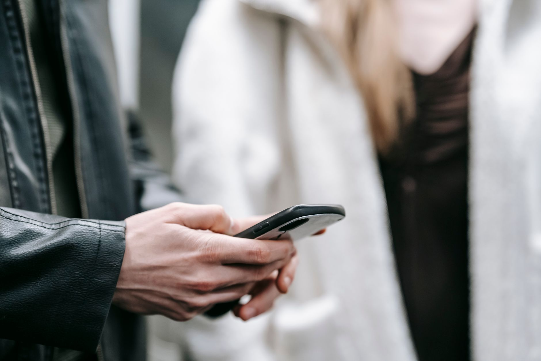 Crop faceless couple in warm clothes standing together while text messaging on phone