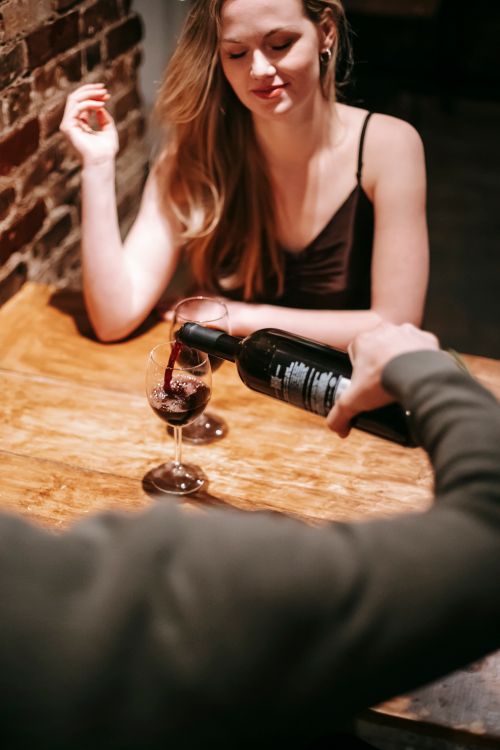 Free Young couple in elegant clothes sitting at table in light bar while having romantic dinner and pouring red wine in glasses Stock Photo