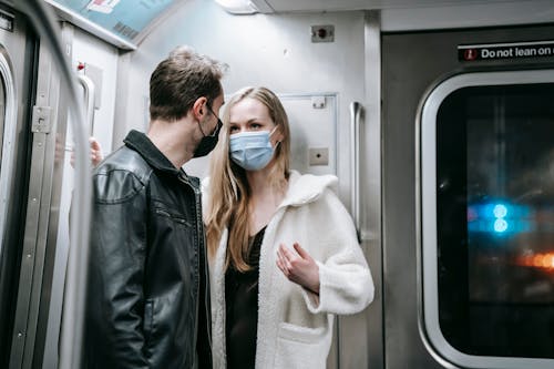 Anonymous couple in warm clothes and protective masks standing in train in subway and talking while looking at each other