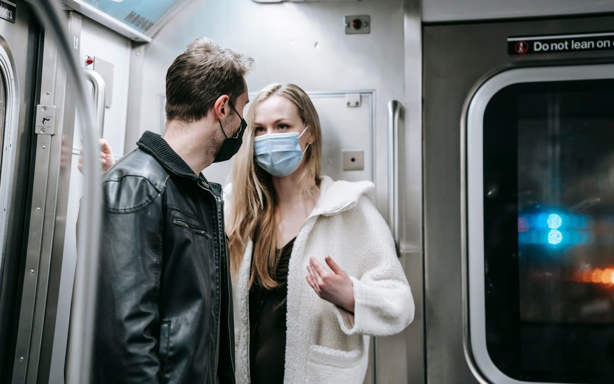 Anonymous couple in warm clothes and protective masks standing in train in subway and talking while looking at each other