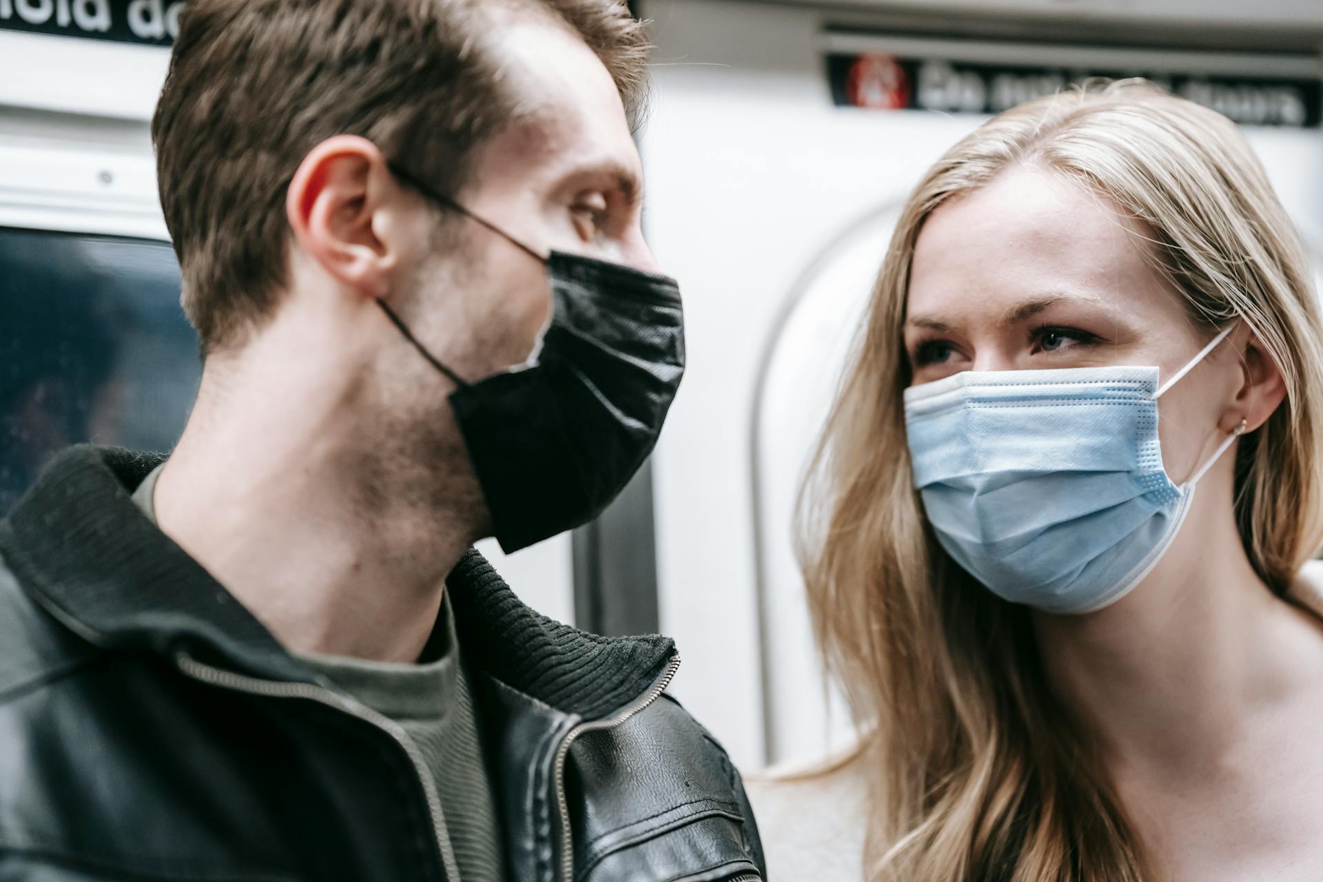 A young couple wearing protective masks conversing on a subway train, highlighting pandemic measures.