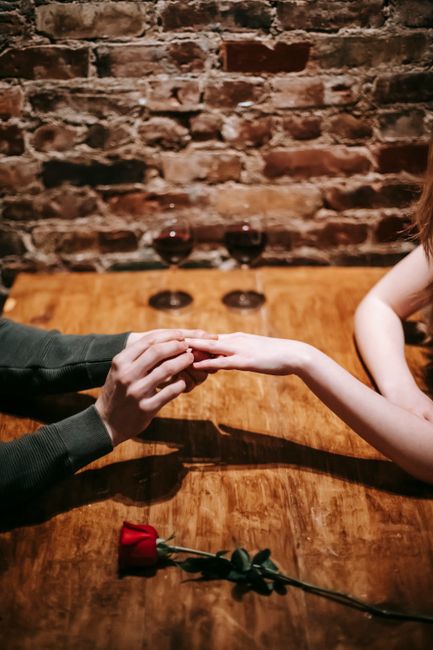 A couple's romantic proposal in a cozy restaurant setting with wine and a single red rose.