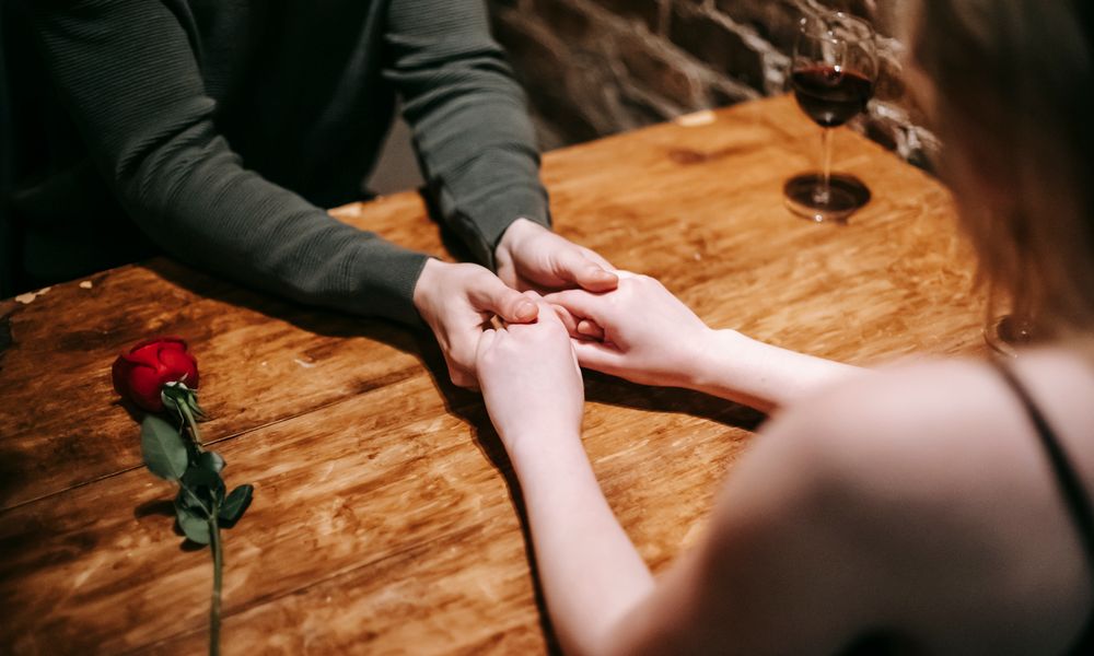 A couple holding hands quietly across a candlelit table, reflecting on their readiness for marriage rather than a fixed date