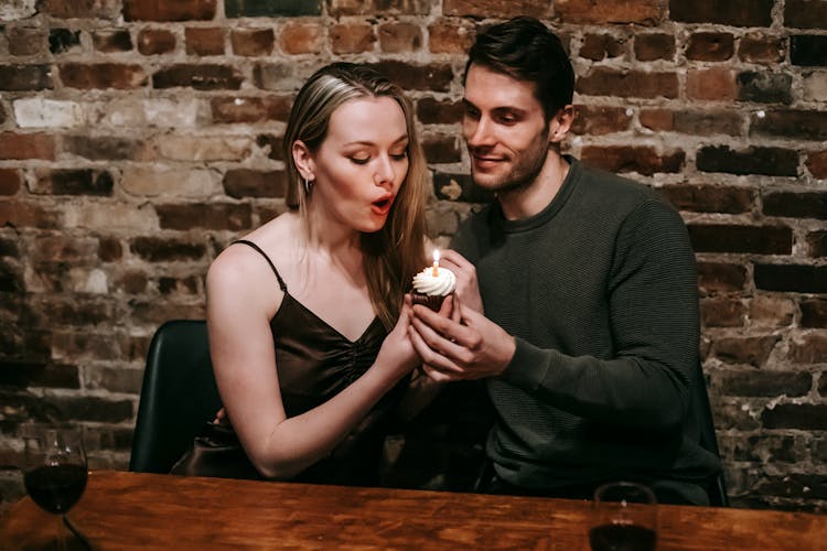 Couple Blows In Candle On Birthday Dessert