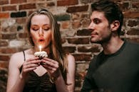 Young couple in elegant outfits in restaurant while blowing in candle on small cupcake and celebrating birthday near brick wall