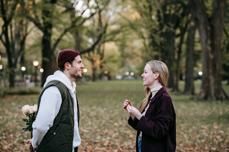 Happy Couple Standing In Street With Flowers Near Trees