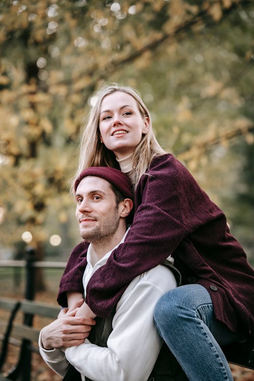 Young couple in warm clothes spending time in street while sitting on bench and embracing in daylight while looking away