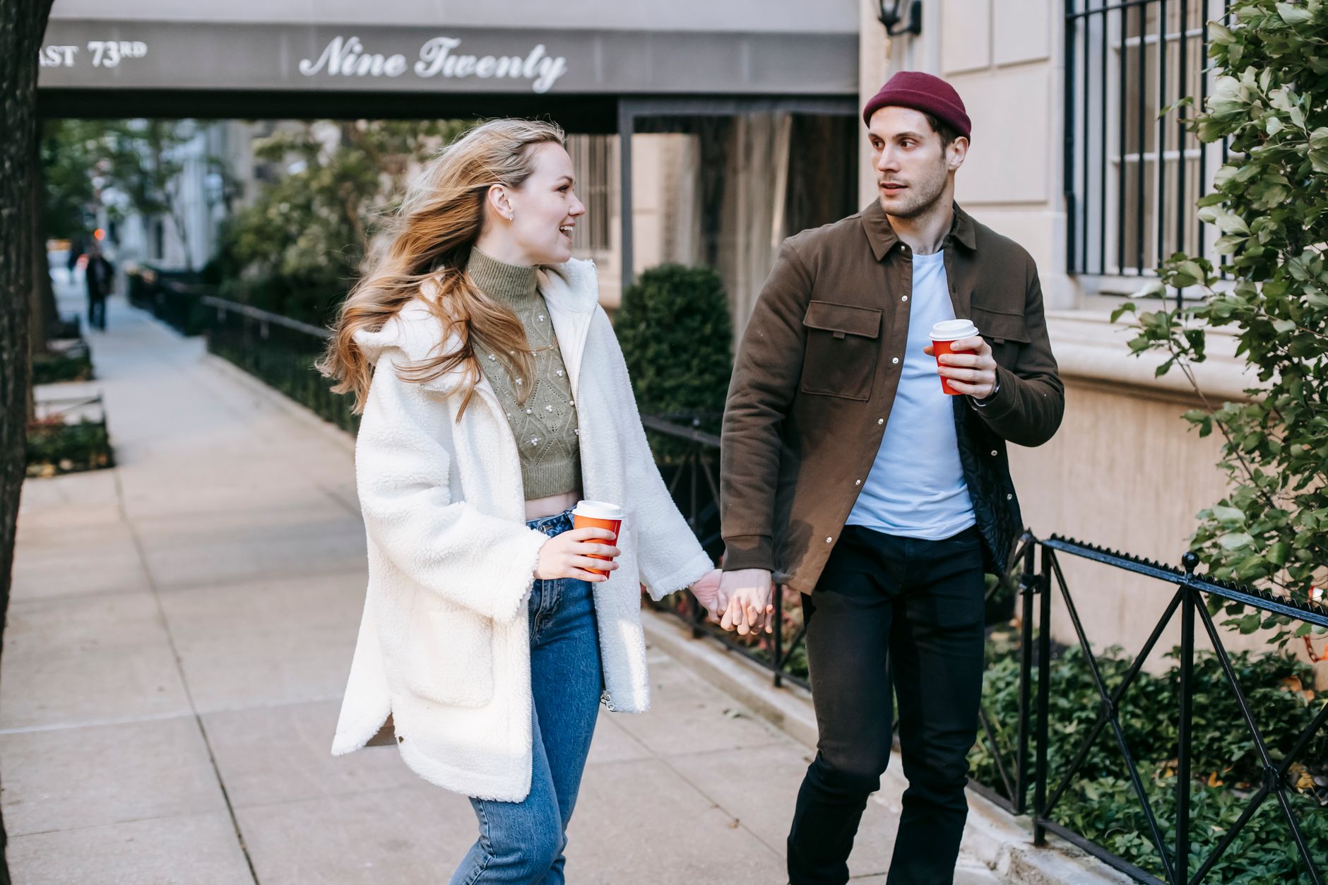 Two people carrying takeaway coffees on a city footpath, the sort of low-cost date that has become its own genre.