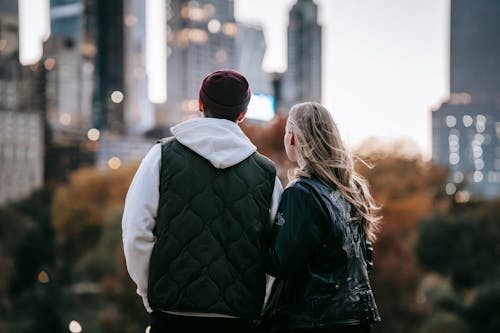 Back view of young couple standing on blurred background of city and enjoying moment