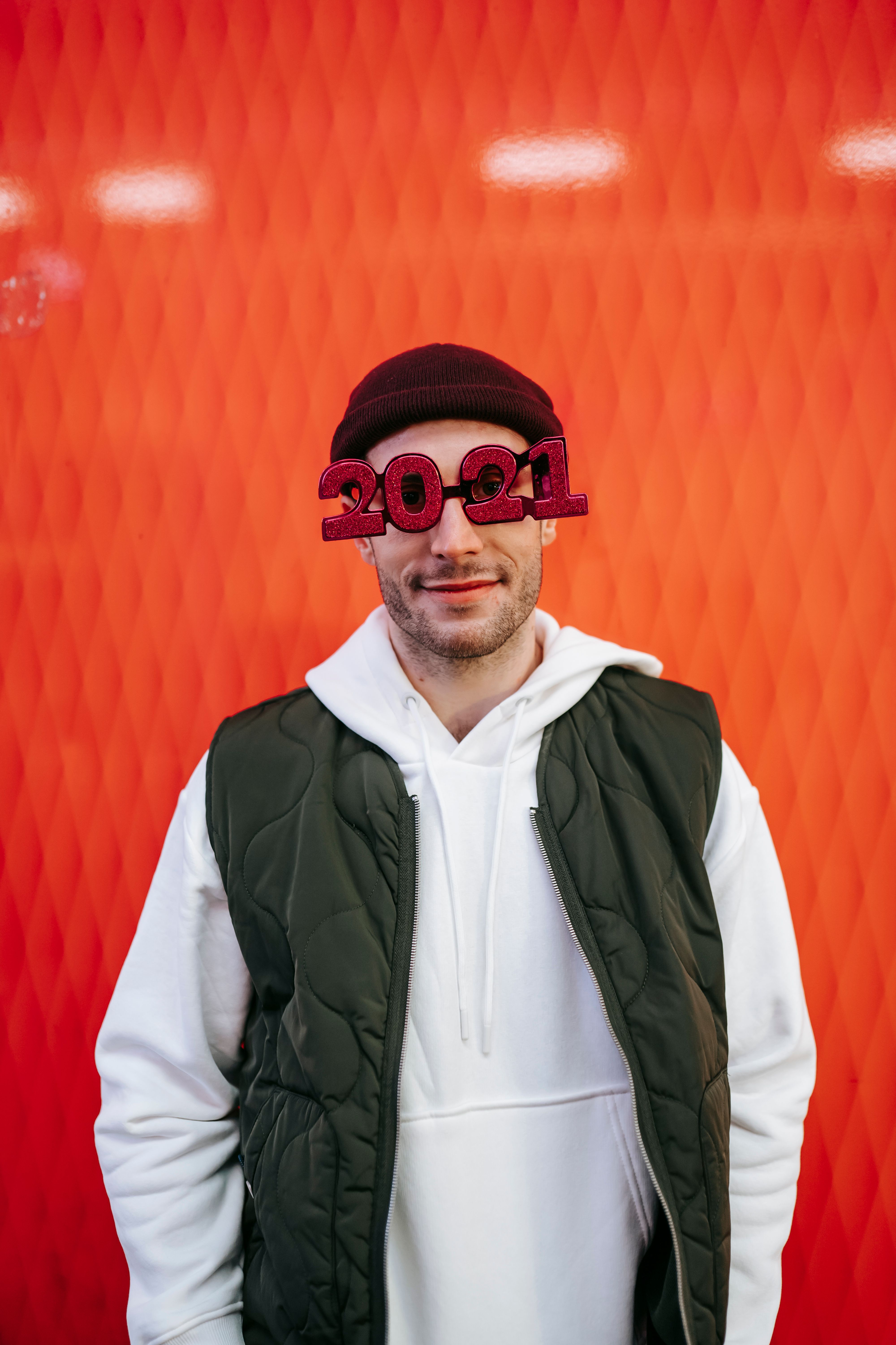 一名开朗的男子站在红色节日背景前，戴着2021年主题眼镜