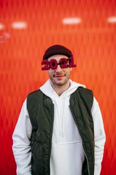 一名开朗的男子站在红色节日背景前，戴着2021年主题眼镜