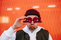 Cheerful male in hat wearing new years festive glasses making face while looking at camera against red wall on street