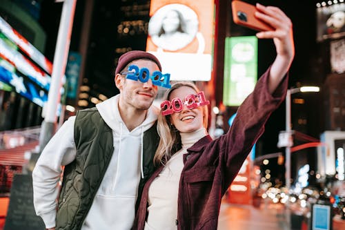 Cheerful couple in trendy glasses taking selfie on street