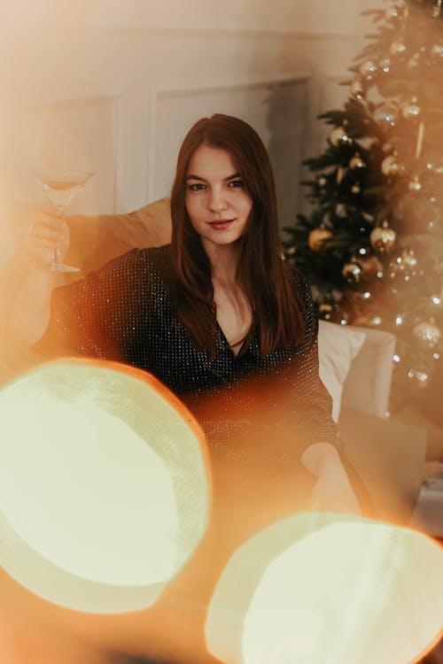 Woman in Black Long Sleeve Shirt Sitting Beside Christmas Tree