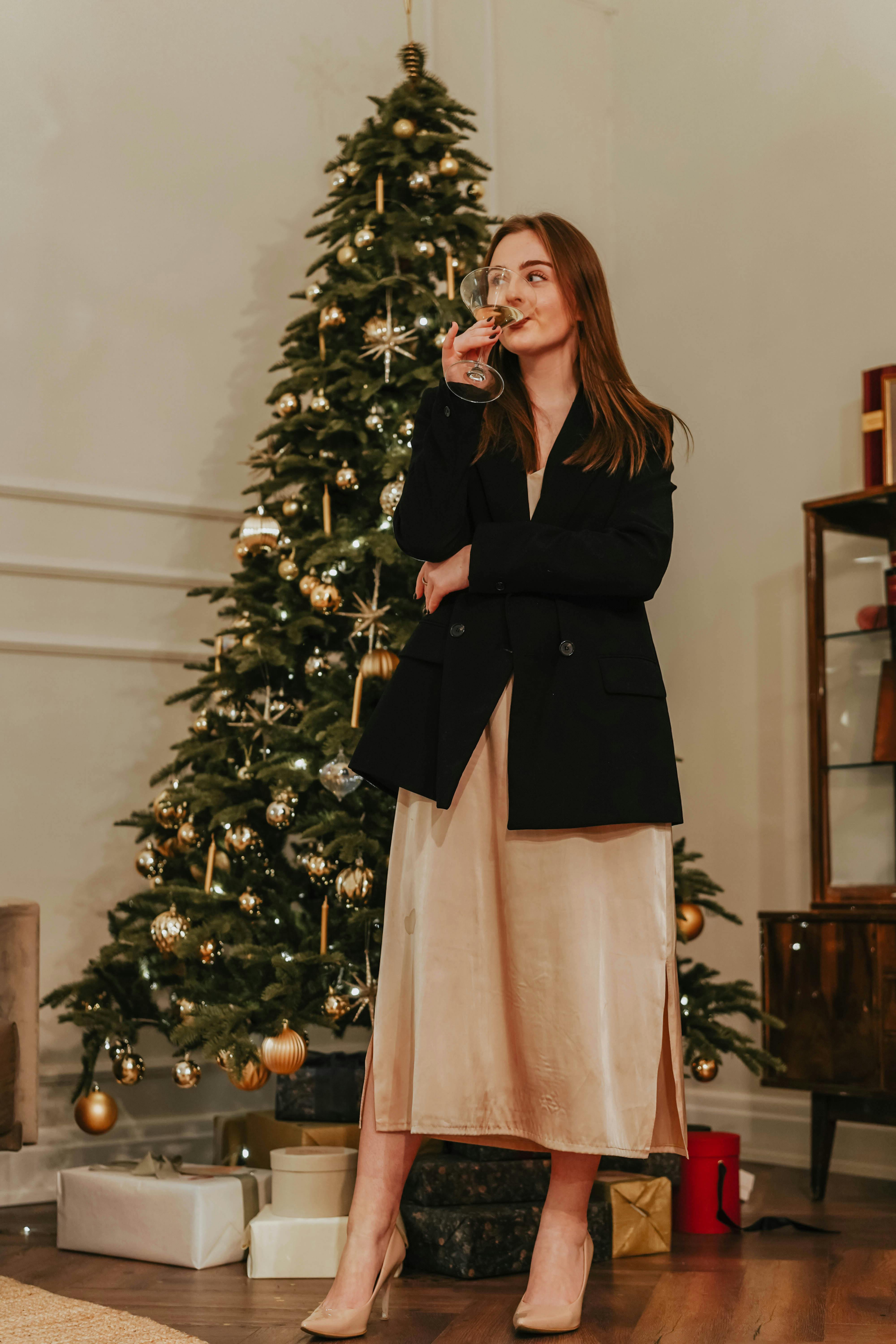 woman in black blazer and skirt standing beside green christmas tree