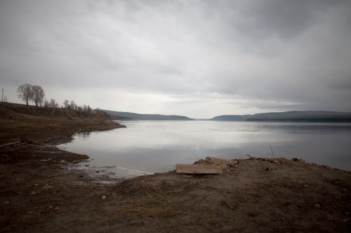 Free Embankment with leafless trees near calm water of vast river under cloudy gray sky Stock Photo