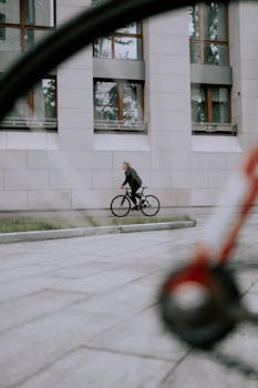 A cyclist rides a bicycle on a city street past a modern building.